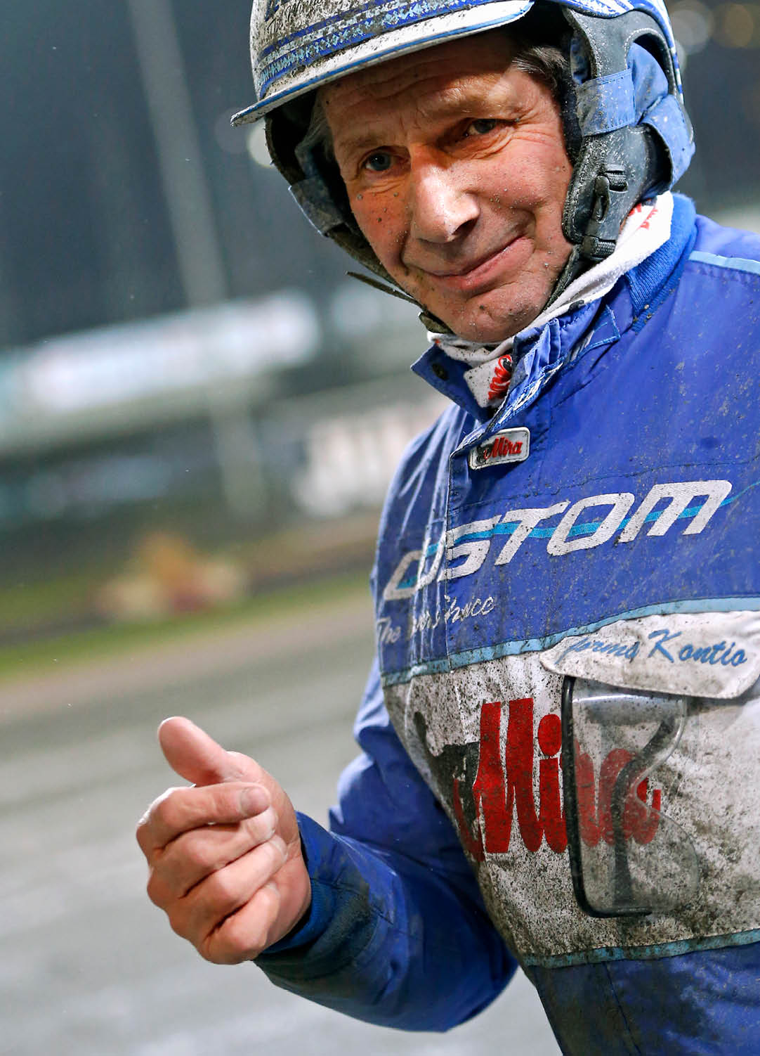 Person wearing a blue racing suit and helmet is giving a thumbs-up gesture with a slight smile. Description generated by AI